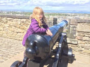 A girl leaning against a cannon with view over edinburgh