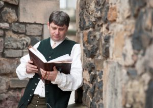 An actor dressed as Robert Burns leaning against a stone wall