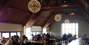 A photograph of a cafe with large windows, timber beams and large circular lights hanging from the ceilings.
