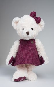 A white toy bear wearing a purple dress and bow