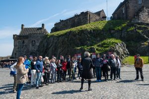 A guided tour stopped near the Governor's House at Edinburgh Castle on a sunny day