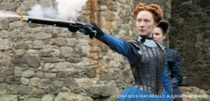 Saoirse Ronan as Mary Queen of Scots in the 2019 cinema production. She is wearing blue period costume and is firing a pistol.