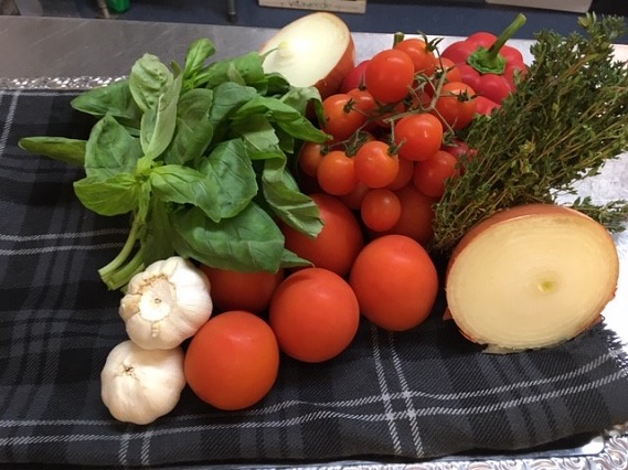 fresh ingredients for soup pictured on a table. Including onion, tomatoes, garlic and basil