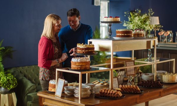 A man and a women browse a table laden with cakes and other treats