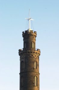 A round tower against a blue sky with a contraption on top.