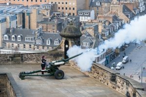 A field gun being fired from the Mills Mount Battery at Edinburgh Castle with a view of Edinburgh and the Forth in the background