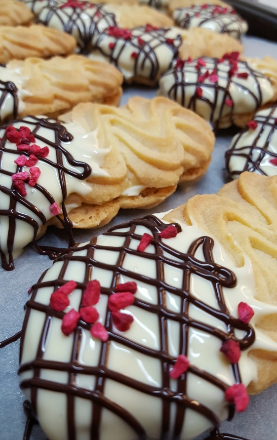 finger biscuits laid out in a row. The bottom half of the biscuits is dipped in white chocolate with a milk chocolate drizzle and red sprinkles