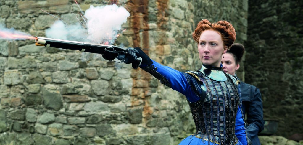 Saoirse Ronan as Mary Queen of Scots in the 2019 cinema production. She is wearing blue period costume and is firing a pistol.