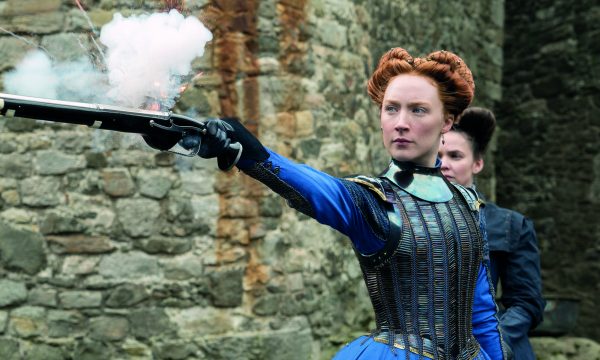 Saoirse Ronan as Mary Queen of Scots in the 2019 cinema production. She is wearing blue period costume and is firing a pistol.