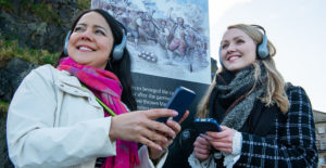 Two young women wearing headphones holding audio guide handsets