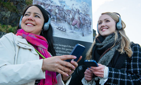 Two young women wearing headphones holding audio guide handsets