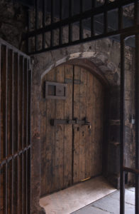 Heavy wooden doors viewed through a heavy metal barred gate.