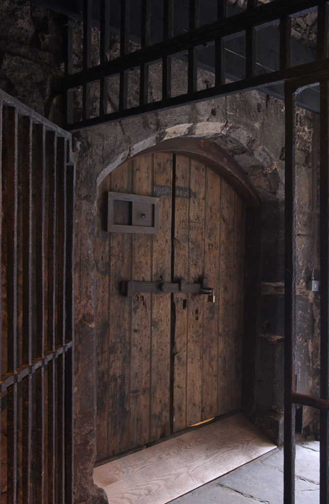 Heavy wooden doors viewed through a heavy metal barred gate.