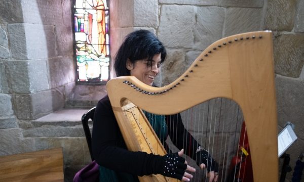 A lady playing a clarsach in fornt of a stained glass window inside Edinburgh Castle
