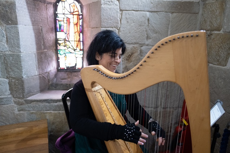 A lady playing a clarsach in fornt of a stained glass window inside Edinburgh Castle