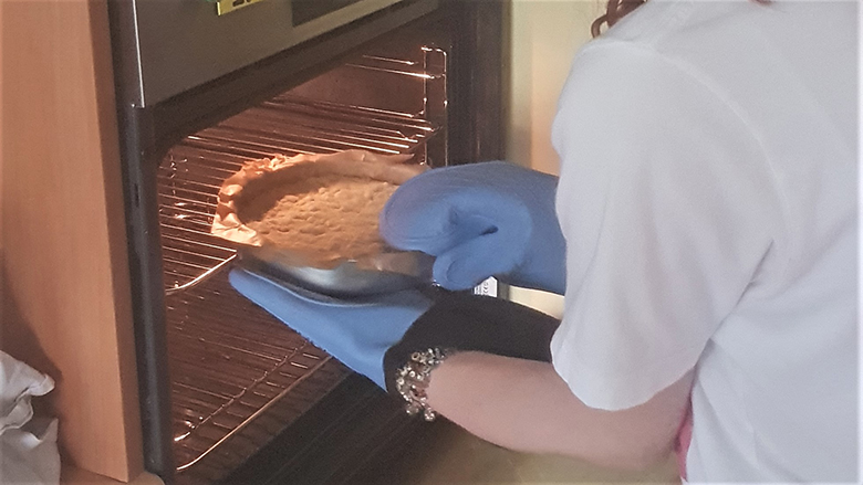 Girl wearing oven gloves removes a round tin of shortbread from the oven.