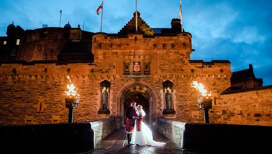A couple pose for a wedding photo at the floodlit gates of Edinburgh Castle
