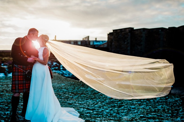 A bride and groom kiss outside Edinburgh Castle with the Bride's veil blowing in the wind