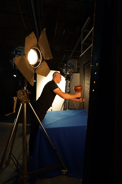 A behind the scenes photo of a stonemason being filmed using traditional tools 