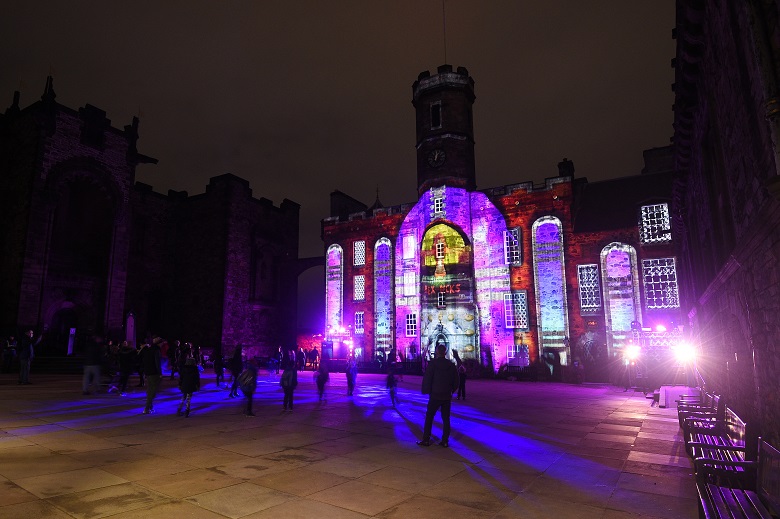 Visitors to Edinburgh Castle looking at a colourful projection on the walls of the royal palace