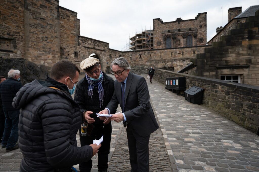 Film still from "The Lost King" showing Steve Coogan and film crew at Edinburgh Castle. 