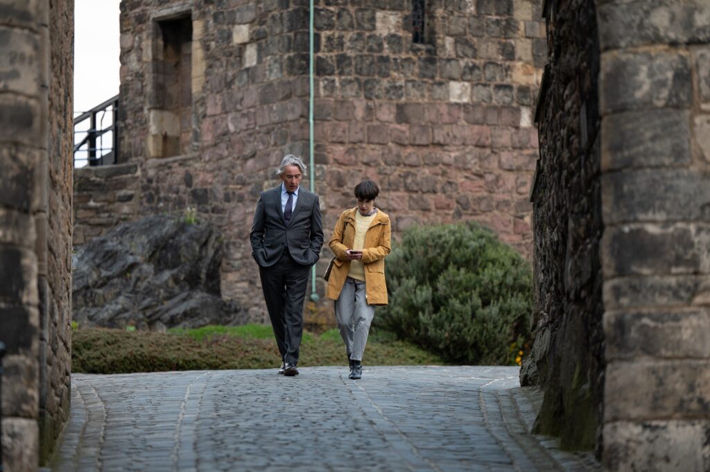 Film still from "The Lost King" showing Sally Hawkins and Steve Coogan walking in the courtyard of Edinburgh Castle. 