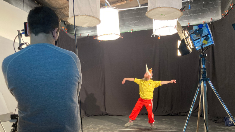 A person in a costume standing on a stage in front of black curtains posing for the camera. 