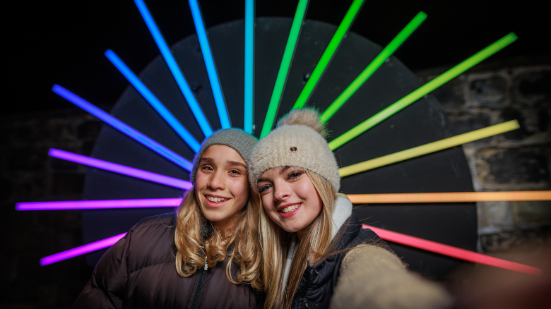 Two people at Edinburgh Castle of Light standing in front of a light installation, smiling at the camera.
