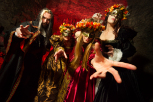 Four people dressed in costumes wearing masks reaching towards the camera. Some of them are also wearing flower crowns.