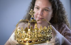 A conservator carefully lifting a lavish gold crown decorated with precious stones