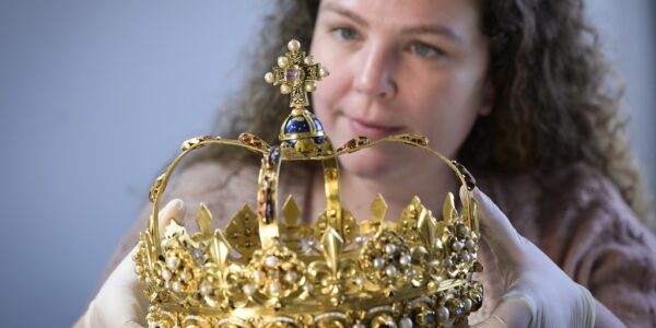 A conservator carefully lifting a lavish gold crown decorated with precious stones