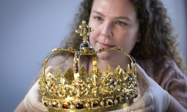 A conservator carefully lifting a lavish gold crown decorated with precious stones