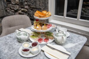 Two set ups for afternoon tea. There is an etagere with scrumptious sandwiches and mini cakes and scones and two teapots.