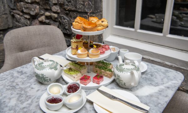 Two set ups for afternoon tea. There is an etagere with scrumptious sandwiches and mini cakes and scones and two teapots.