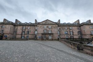 Ornate old building with a courtyard outside it under a grey sky.