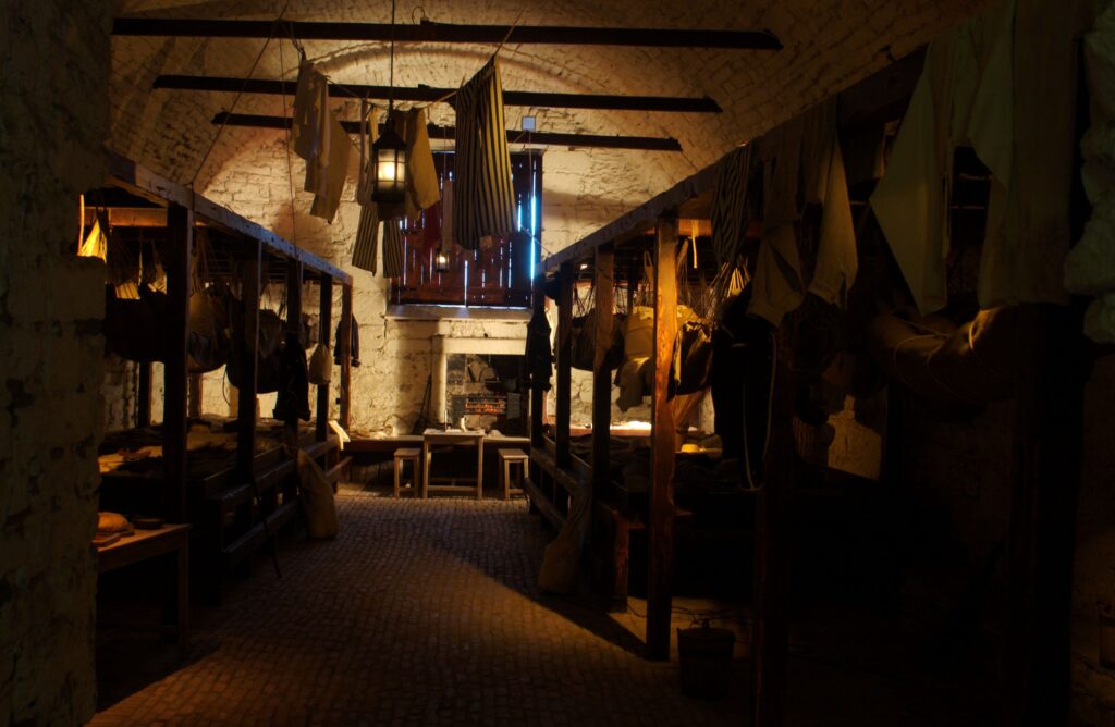 Reconstruction of a historic prison room with hammocks and clothing in dingy lighting.
