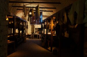 Reconstruction of a historic prison room with hammocks and clothing in dingy lighting.
