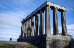 Grecian pillars in a half square formation on top of a hill with people standing beside them.